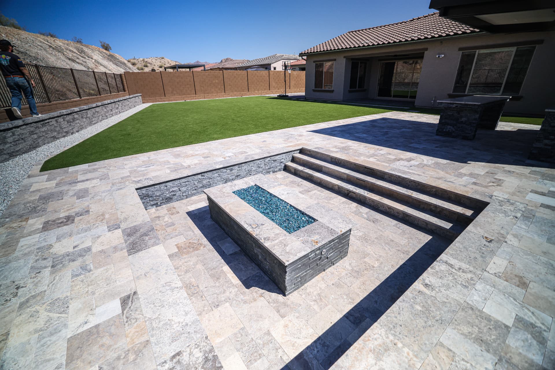 Sunken travertine patio with stone steps and a glass fire pit feature