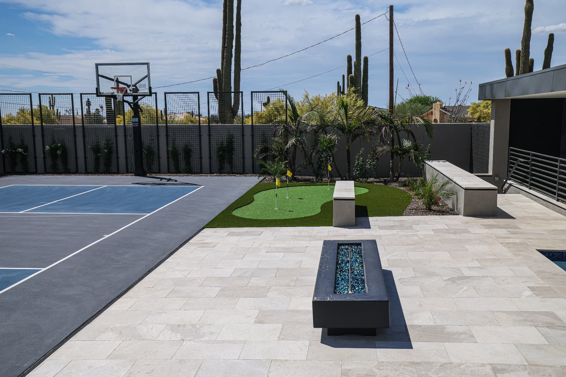 Sport court beside a travertine patio with linear fire table and putting green