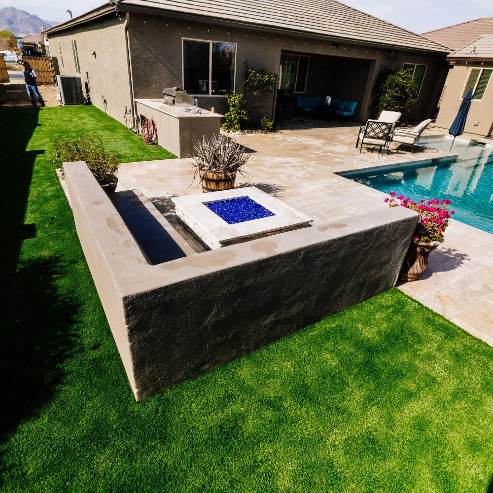 Backyard fire pit with blue glass surrounded by turf and pool