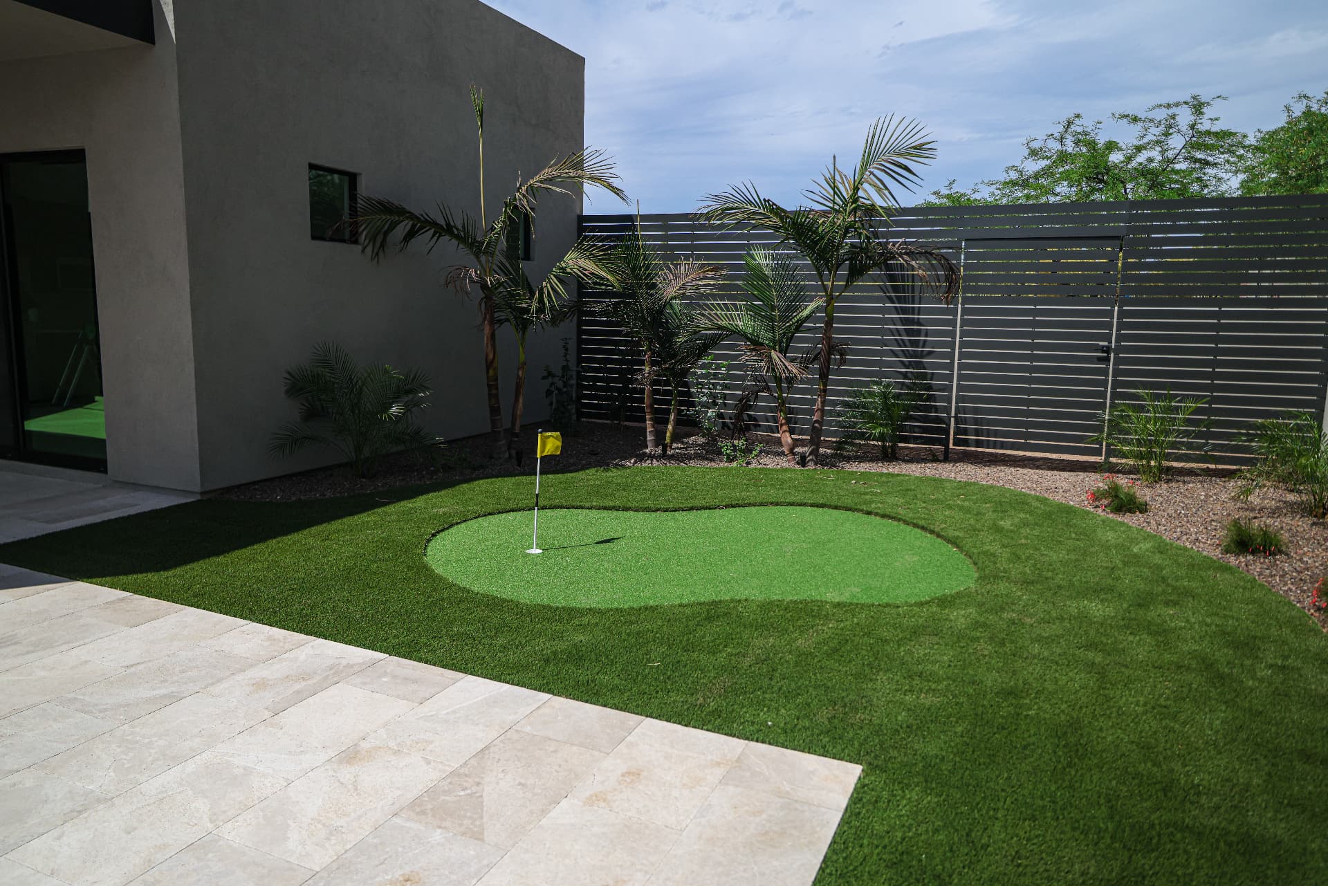 Custom backyard putting green edged by travertine and desert landscaping