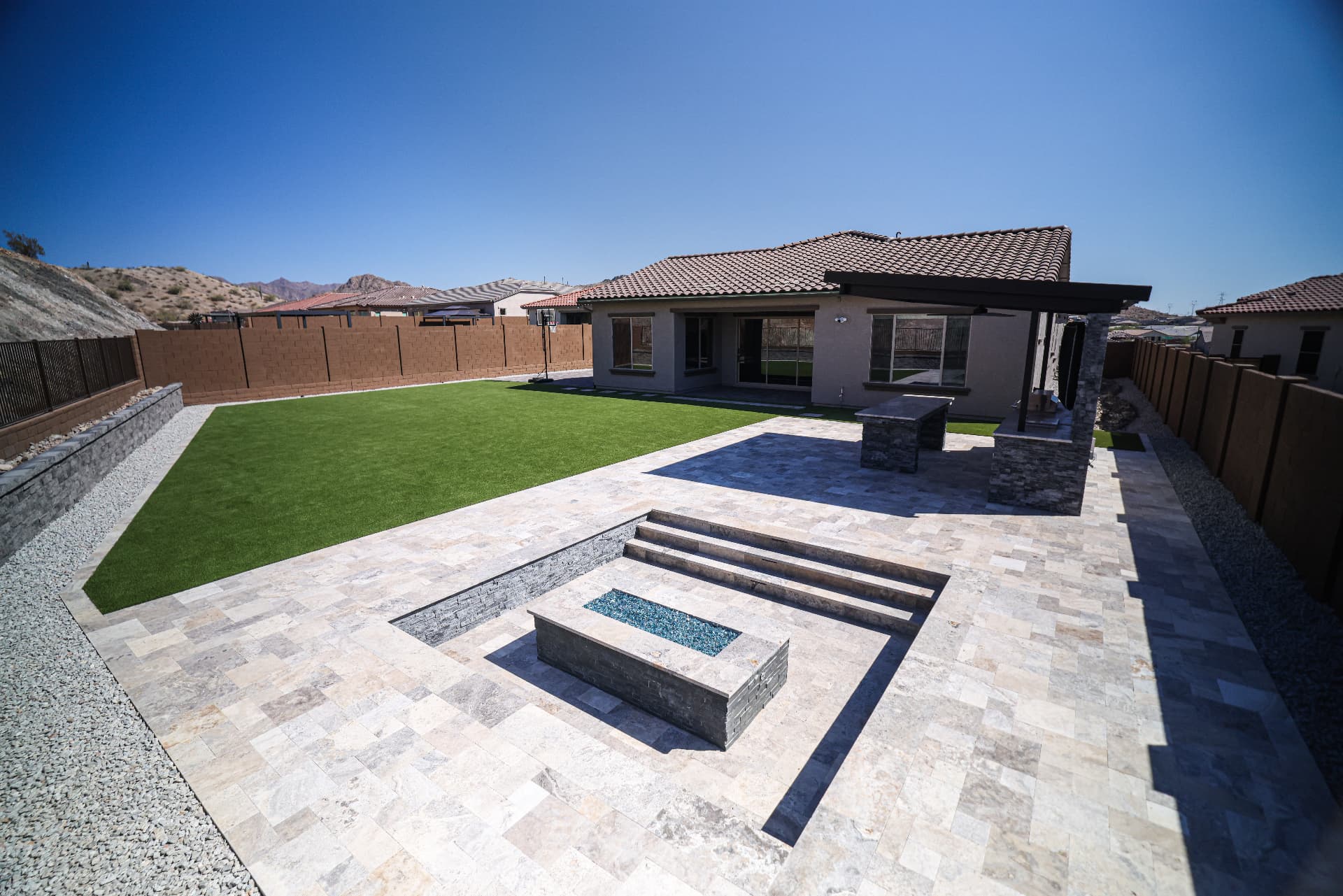 Backyard with artificial turf lawn, travertine patio, and sunken fire pit lounge